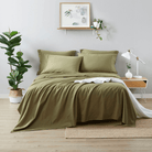 Green bedding set on a bed in a bedroom with plants and decor.