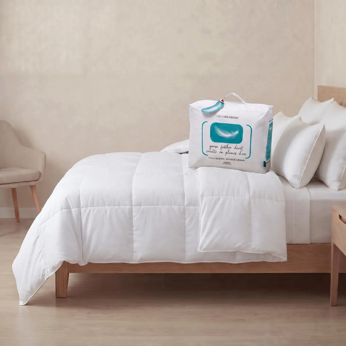A White Goose Feather Duvet set on a wooden bed frame with matching white pillows, alongside its white packaging bag featuring a blue whale graphic.