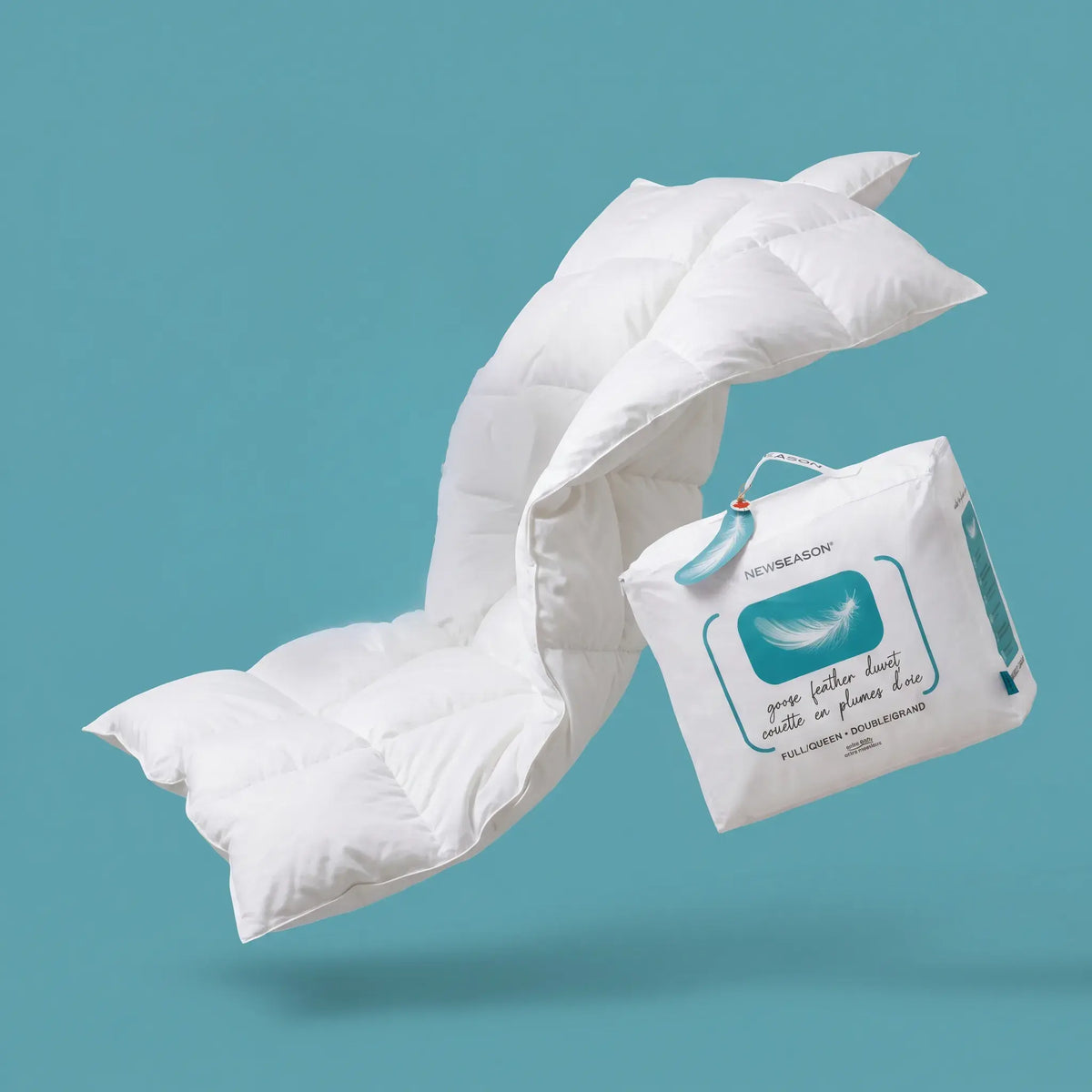 A white down-style quilted comforter or pillow is shown floating against a teal background, alongside its branded white storage bag. The bag has a teal graphic and text that appears to read 'NOTSEASON' and 'your feather dream starts in dreams like this.
