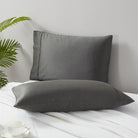 Two gray Classic 500 Thread Count Organic Pillowcase Pair on a white bed with a plant in the corner.