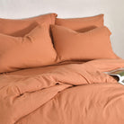 Orange bedding set with Bamboo Linen Pillowcase Pairs on a bed against a white wall.