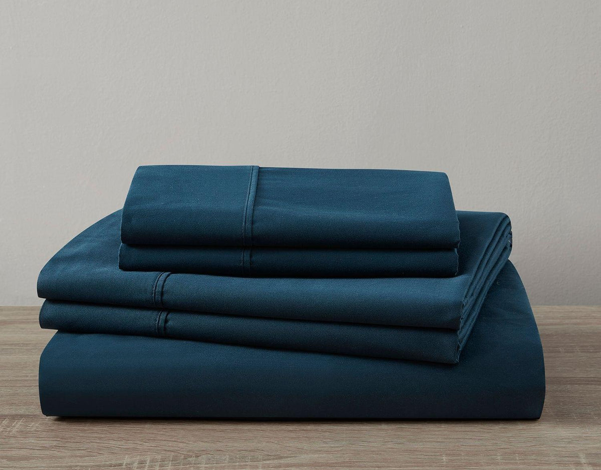Set of blue bed sheets stacked on a wooden surface with a neutral background