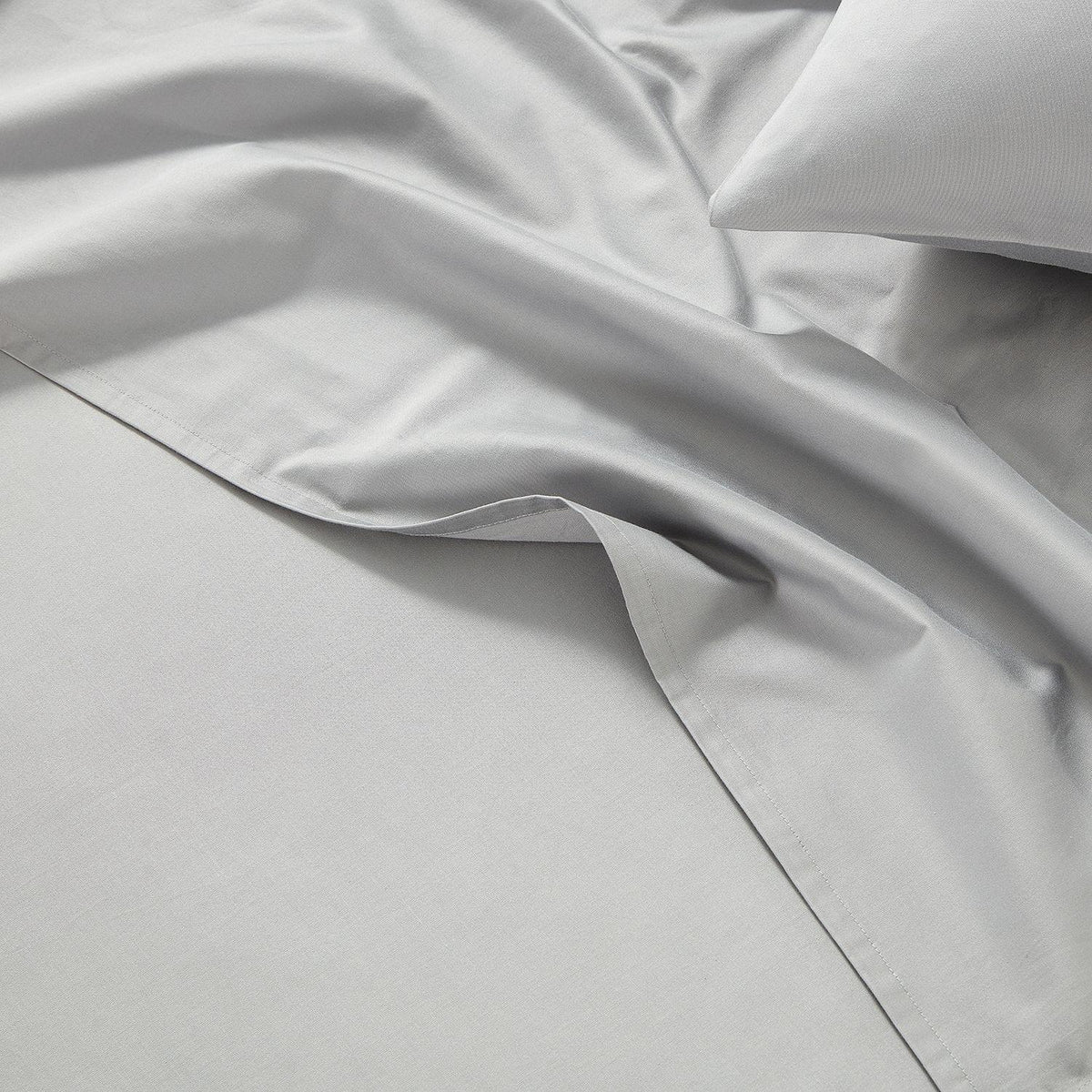 Close-up of light gray bedding with a pillow on a bed.