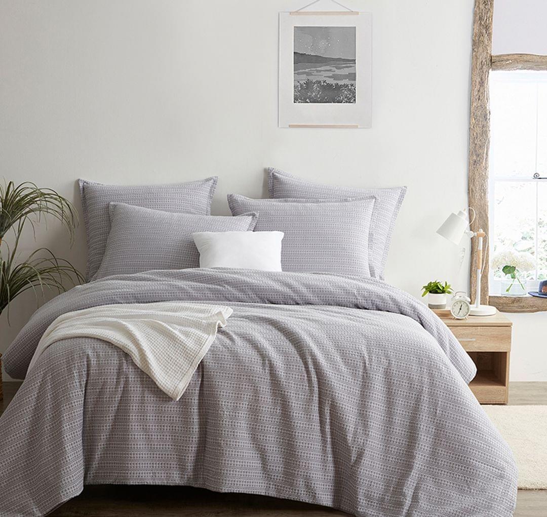 Gray checkered Seersucker Euro Sham set on a bed in a bright bedroom with a plant and framed picture.